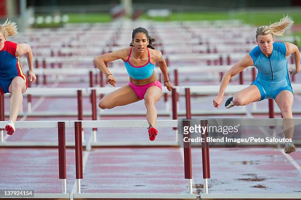 runners jumping hurdles in race - hurdling track event stock-fotos und bilder