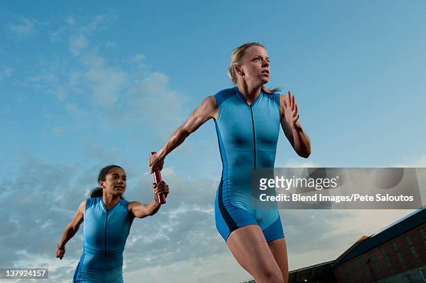runners passing baton in relay race - staffel stock-fotos und bilder