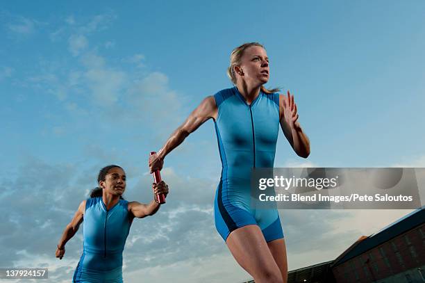 runners passing baton in relay race - relay fotografías e imágenes de stock