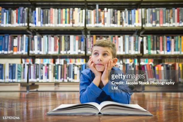 hispanic boy laying on library floor reading book - melbourne school stock pictures, royalty-free photos & images