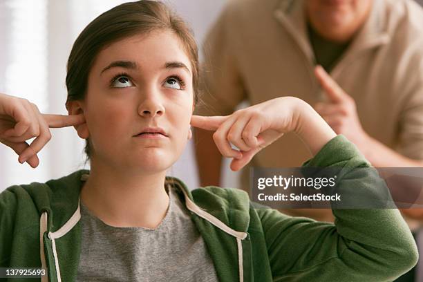 daughter with fingers in ears as father scolds - vingers in de oren stockfoto's en -beelden