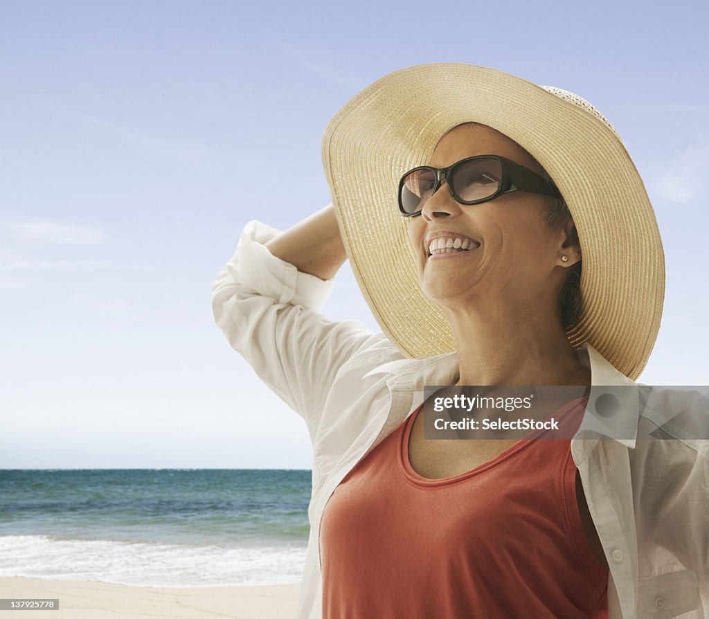 Woman standing on the beach holding hat against the wind