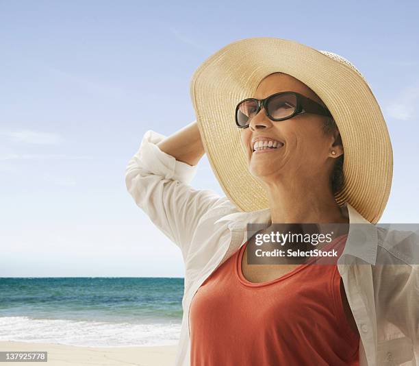 woman standing on the beach holding hat against the wind - a woman wear hat and sunglasses stock pictures, royalty-free photos & images