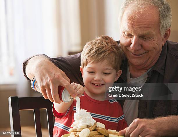 grandfather and grandson using whipped cream on waffles - slagroom stockfoto's en -beelden
