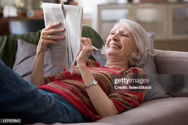 elderly woman doing newspaper crossword puzzle - kruiswoordpuzzel stockfoto's en -beelden