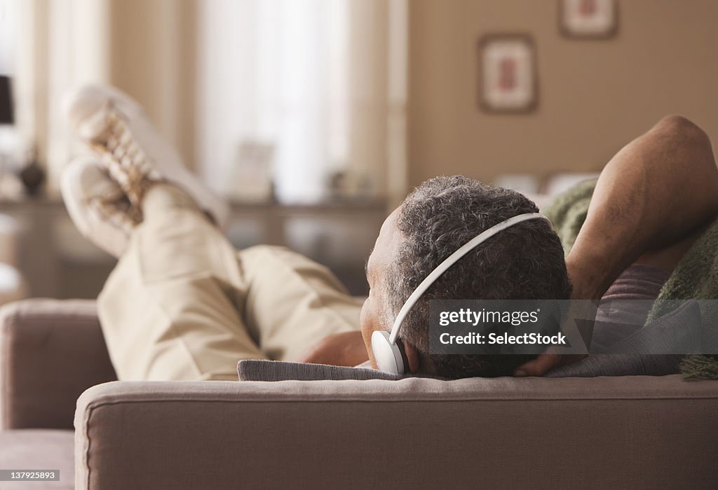 Hombre mayor envenenado sentar en un sofá con auriculares