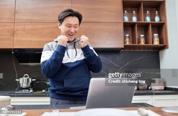 an east asian man holds a laptop in his hand in the family kitchen, and his face shows a surprised expression - 僅一男人 stockfoto's en -beelden