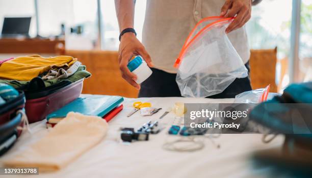 la mano de un hombre empaca cosméticos y medicamentos para el viaje en una bolsa con cremallera. - bolsa de cor creme fotografías e imágenes de stock