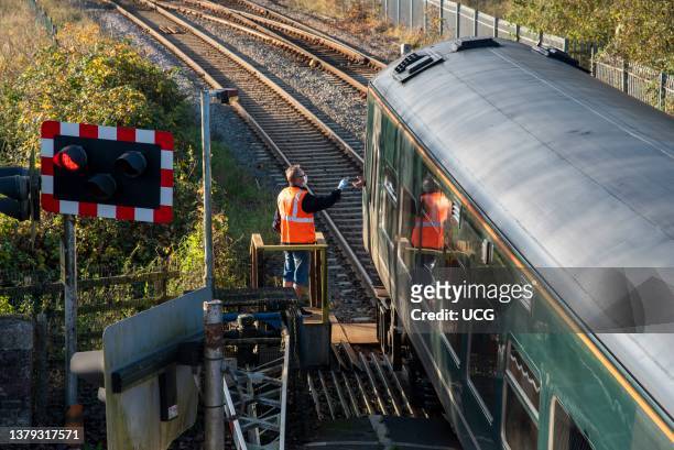 Crediton, Devon, England, UK, Signalman presents a key to the train driver at Crediton station. The key gives the train driver access onto a single...