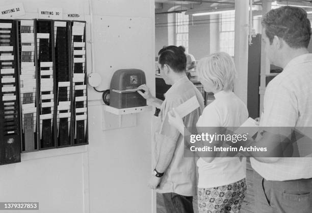 View of workers registering a shift using a punch clock at a knitting factory, Boston, Massachusetts, 1971.