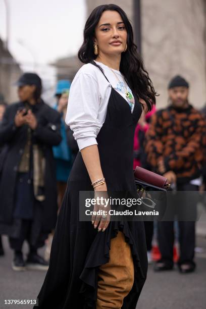 Amina Muaddi wearing a printed t-shirt, black dress, burgundy Loewe bag and beige over the knees boots, is seen outside Loewe, during Paris Fashion...