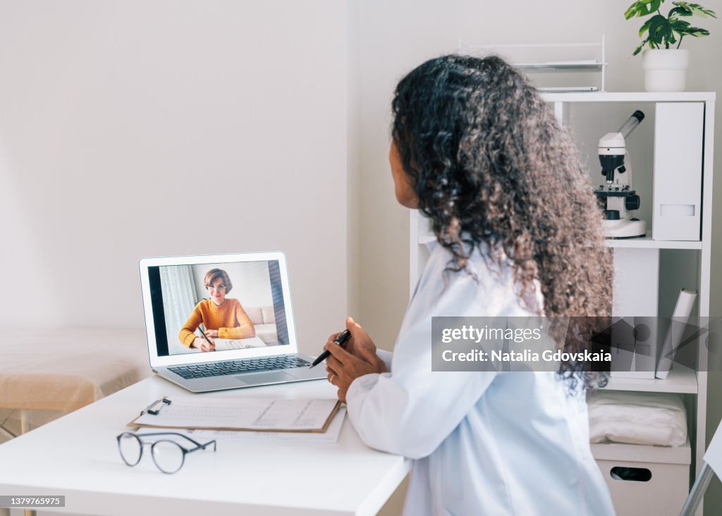 Faceless african-american doctor using laptop for telecommunication with sick patient on quarantine