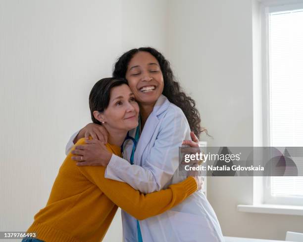 african-american doctor embracing mature female patient at clinical appointment. establishing trust - doctors embracing stock pictures, royalty-free photos & images