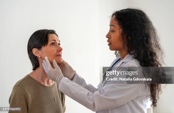 worried african-american doctor examining patient glands, oncology concerns. laryngologist checkup - schildklier stockfoto's en -beelden