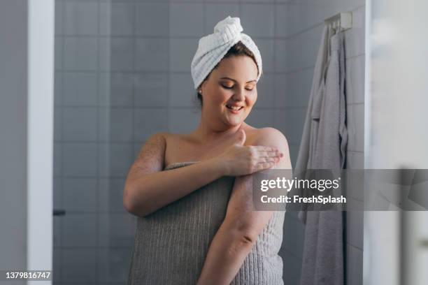beautiful plus size woman applying body lotion after taking a shower - applying sunscreen stock pictures, royalty-free photos & images