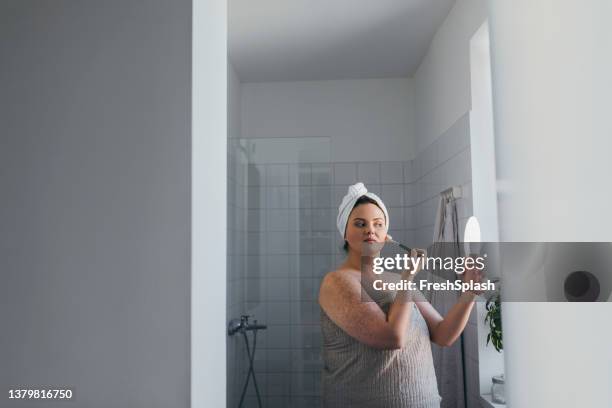 beautiful overweight caucasian woman applying makeup in the bathroom - woman shower bath imagens e fotografias de stock