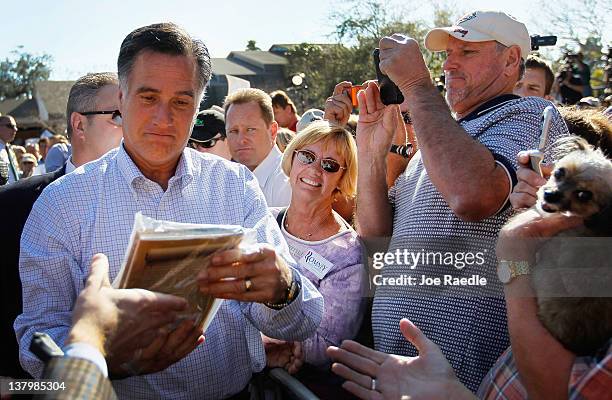 Republican presidential candidate and former Massachusetts Gov. Mitt Romney looks at a book given to him as he greets people during a rally with...