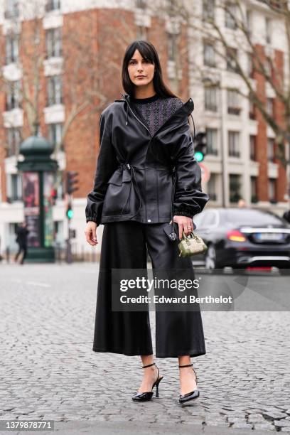 Leia Sfez wears a black and purple logo print pattern pullover from Loewe, a black shiny leather oversized belted jacket, black shiny leather wide...