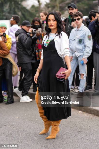 Amina Muaddi wears gold bracelets, a white with multicolored print pattern long sleeves t-shirt, a black V-neck / tank-top / ruffled borders...