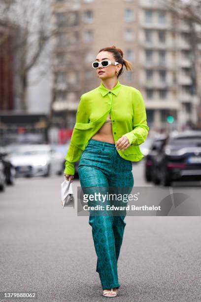 Merve Gorgoz wears white sunglasses from Versace, a green shirt, dark green and blue shiny leather snake print pattern large pants, a white shiny...
