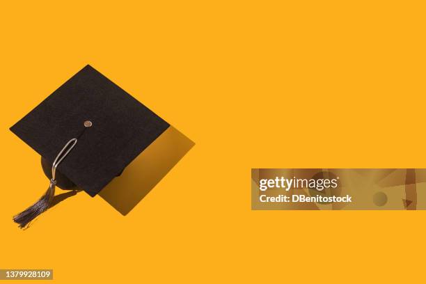 black graduation cap with gray tassel with hard shadow, on the left side, on yellow background. graduation, achievement, goal, degree, master, bachelor, university, college and success concept. - birrete fotografías e imágenes de stock