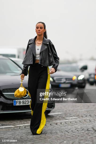 Guest wears gold earrings, a gold and silver chain necklace, a black shiny leather zipper biker jacket, a gray V-neck / cropped tank-top from Loewe,...