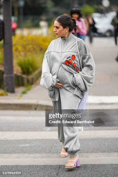 Guest wears gold pendant earrings, a pale gray zipper oversized with orange print pattern sweater from Loewe, matching pale gray sport pants from...