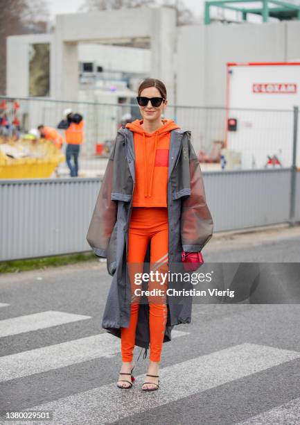 Gala Gonzalez seen wearing grey see trough Loewe rain coat, orange hoody, pants with logo print, red micro bag, heeled sandals outside Loewe during...