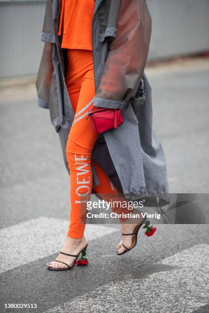 Gala Gonzalez seen wearing grey see trough Loewe rain coat, orange hoody, pants with logo print, red micro bag, heeled sandals outside Loewe during...