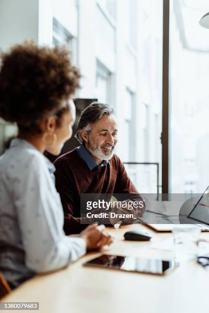 smiling financial advisor and business person talking to mixed race female colleague in office - business meeting stock pictures, royalty-free photos & images