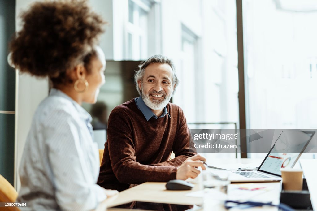 Smiling financial advisor and business person talking to mixed race female colleague in office
