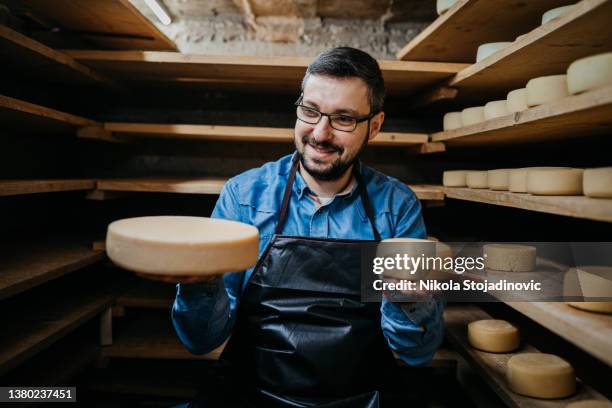 handsome cheesemaker is checking cheeses in his workshop storage - cheese maker stock pictures, royalty-free photos & images