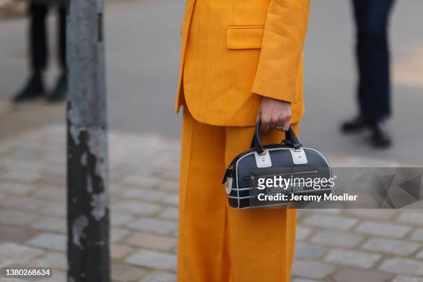 Fashion Week guest seen wearing an orange suit, dior bowling bag and white heels on March 03, 2022 in Paris, France.