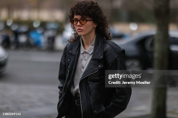 Fashion Week guest is wearing a black leather jacket, grey blouse and a brown retro sunglasses on March 03, 2022 in Paris, France.