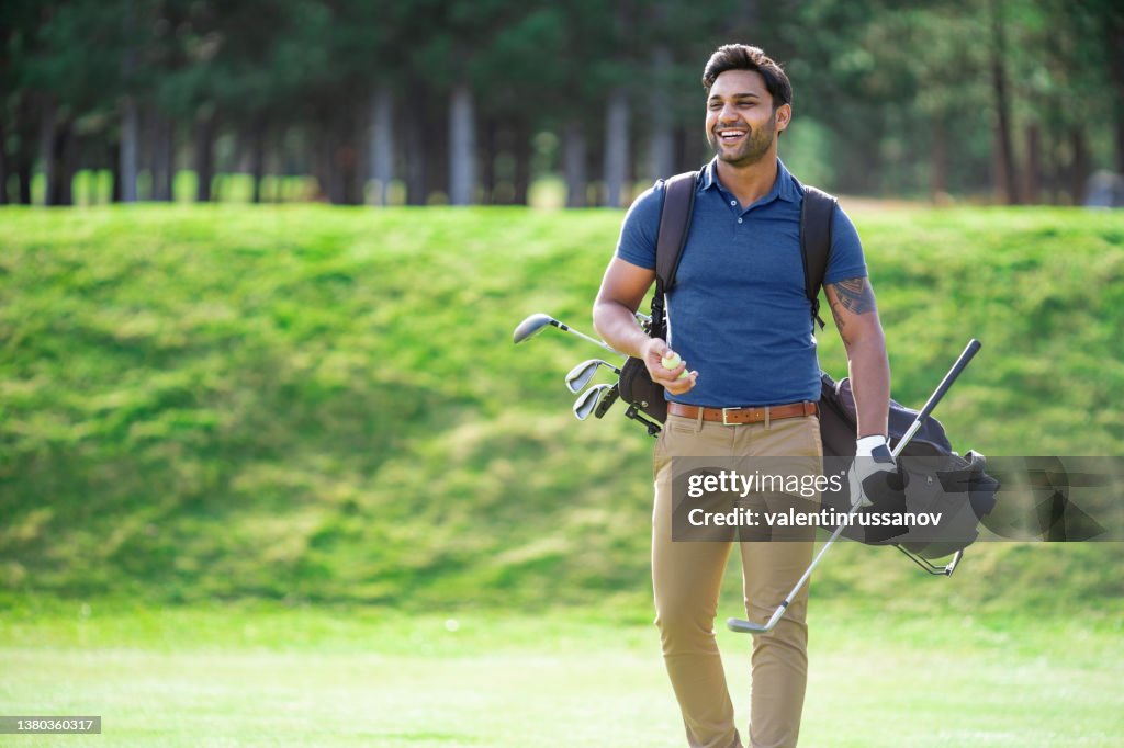 Indian ethnicity smiling golf player walking on the course and carrying his golf clubs