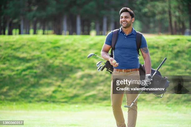 indian ethnicity smiling golf player walking on the course and carrying his golf clubs - golfer stock pictures, royalty-free photos & images