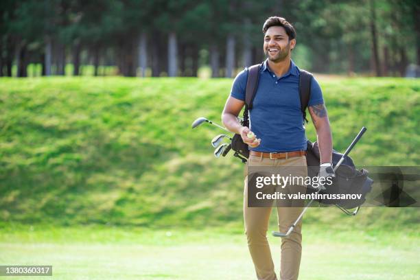 etnia indiana sorrindo jogador de golfe andando no campo e carregando seus tacos de golfe - golfer - fotografias e filmes do acervo