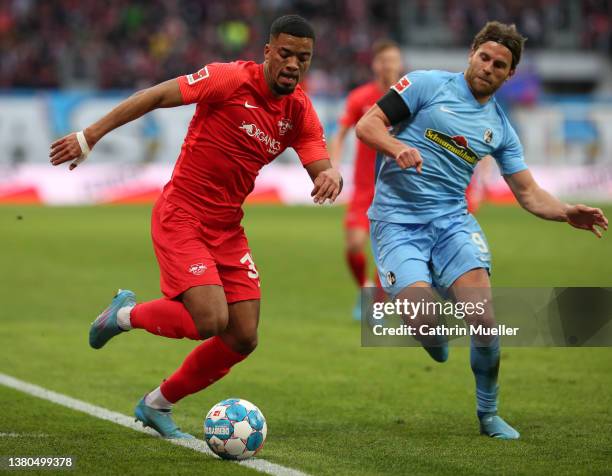 Benjamin Henrichs of RB Leipzig runs with the ball whilst under pressure from Lucas Hoeler of SC Freiburg during the Bundesliga match between RB...