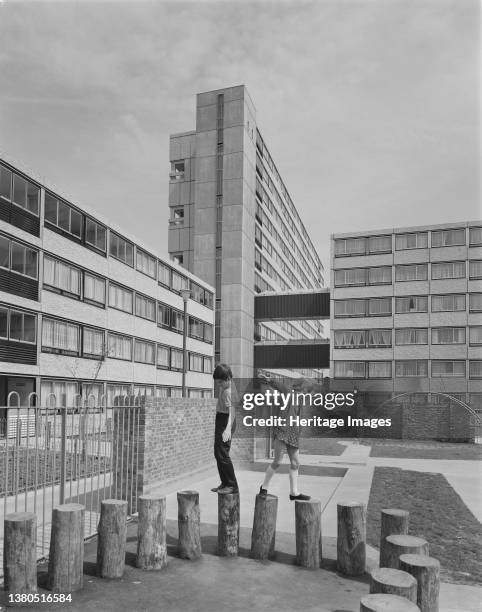 Pooles Park, Finsbury Park, Islington, London, . Two children playing on posts in a playground besides blocks of flats at Pooles Park, built using...
