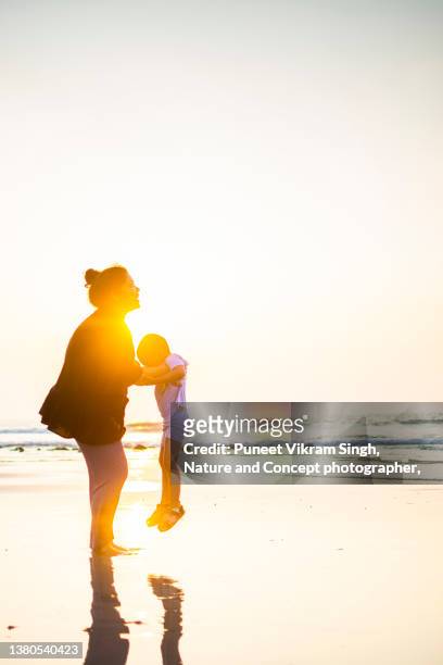 a playful mother throwing her son in the air at a beach - dad throwing kid in air stockfoto's en -beelden