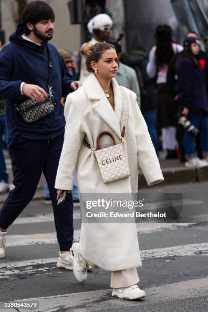 Guest wears gold earrings from Dior, a gold chain pendant necklace from Chanel, a brown pullover, beige denim large pants, white and beige leather...