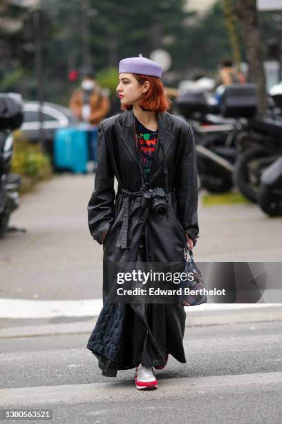 Guest wears a pale purple felt beret, a black with red and green print pattern t-shirt, a black shiny leather oversized long coat, black shiny...