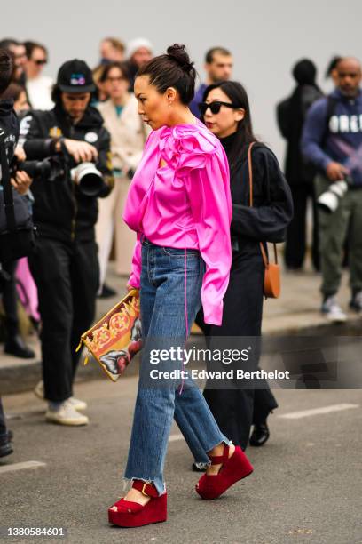 Guest wears gold earrings, a neon pink silk puffy sleeves / embroidered flower blouse, blue denim large pants, red suede strappy platform / wedge...