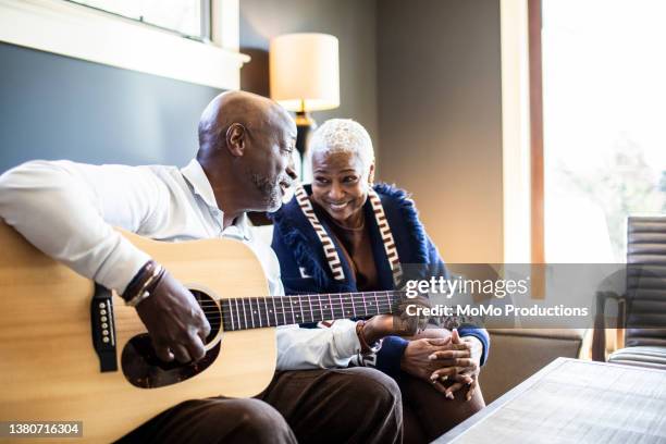 senior man playing acoustic guitar for his wife at home - playing music together stock-fotos und bilder