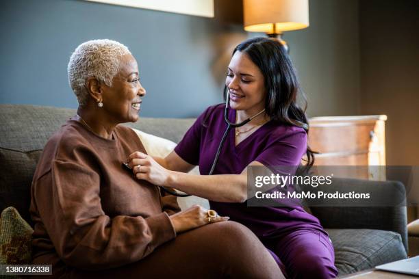 nurse checking senior woman's vital signs in her home - color day productions stockfoto's en -beelden