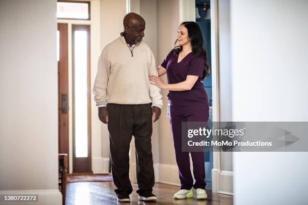 in-home nurse helping senior man walk down hallway - black pants stockfoto's en -beelden