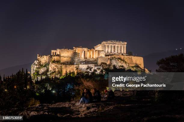 people on pnyka hill and the acropolis of athens, greece at night - acropolis athens stock pictures, royalty-free photos & images