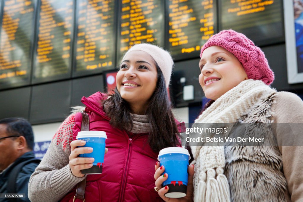 Women holding coffees in train station.