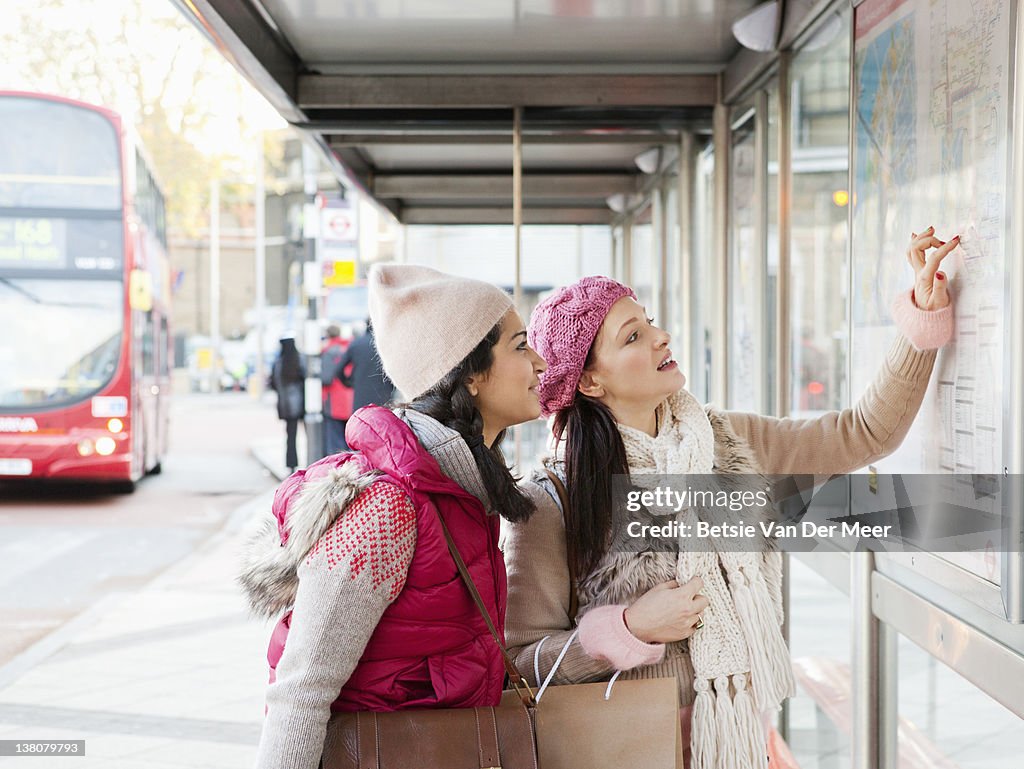 Two women looking at bus route map at bus stop.