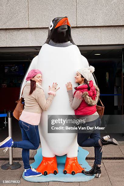 two women hugging large penguin. - big hug stock pictures, royalty-free photos & images